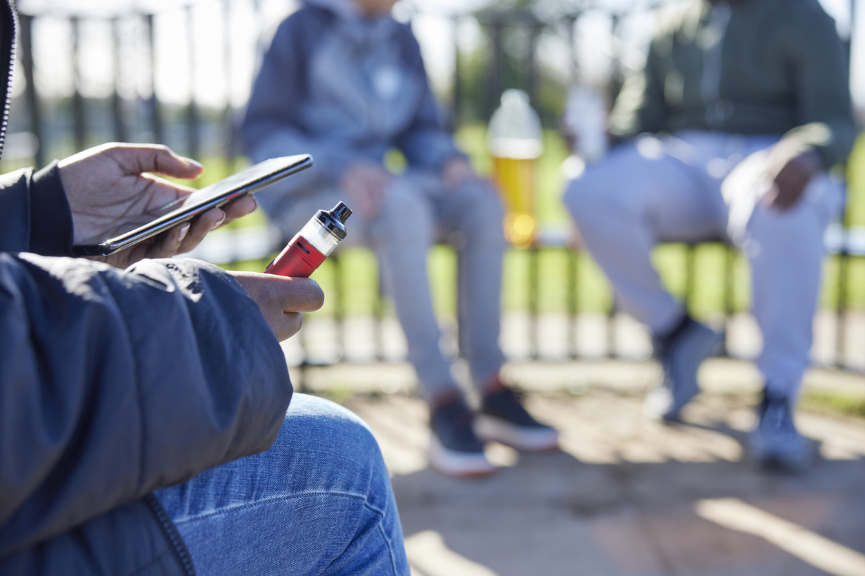 A group of young adults socialising, with one person using a vape.