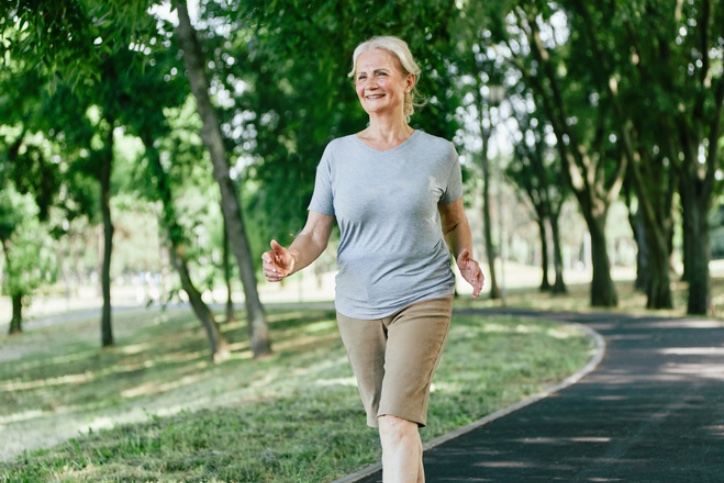 An older adult walking on a path in a green park.