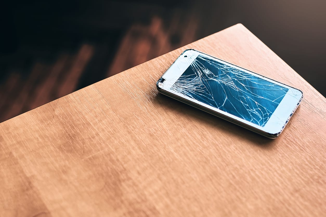 A smartphone with a cracked screen on a table.