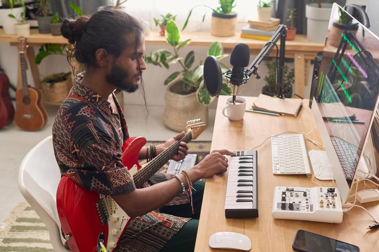 An independent musician playing guitar in a small studio.